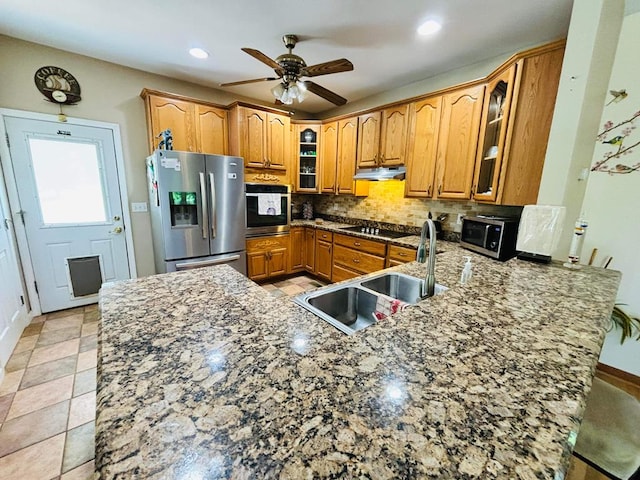 kitchen with brown cabinetry, glass insert cabinets, a peninsula, stainless steel appliances, and under cabinet range hood