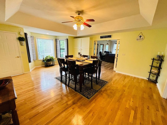 dining space featuring light wood-style floors, baseboards, and a tray ceiling