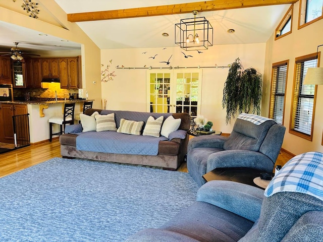 living area featuring plenty of natural light, lofted ceiling with beams, light wood finished floors, and ceiling fan with notable chandelier