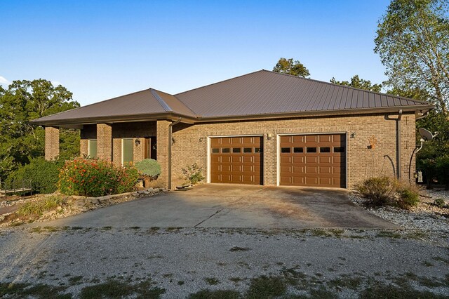 view of front of home featuring a garage, metal roof, brick siding, and driveway