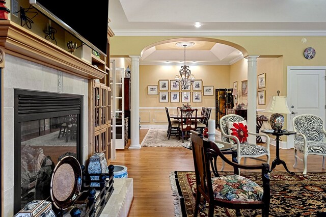 dining room featuring arched walkways, light wood-style floors, a raised ceiling, and ornate columns