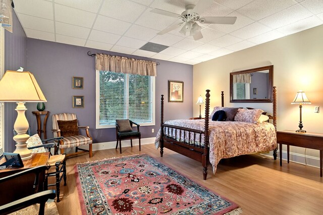 bedroom with a paneled ceiling, ceiling fan, baseboards, and wood finished floors