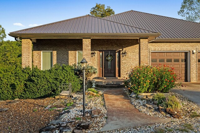 view of front of home with a garage, driveway, metal roof, and brick siding