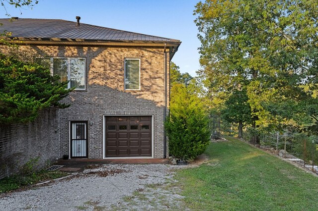 view of side of property with a garage, brick siding, a yard, and driveway