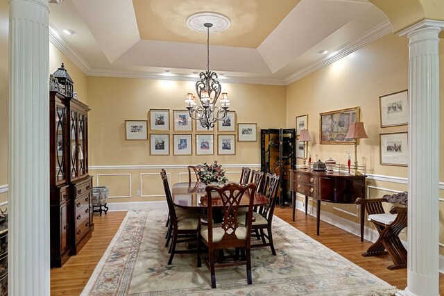 dining room with arched walkways, light wood-style floors, wainscoting, a tray ceiling, and decorative columns