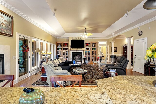 living room with arched walkways, a fireplace, ornamental molding, a tray ceiling, and decorative columns