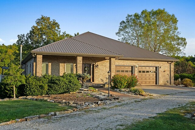 ranch-style house with driveway, a garage, metal roof, and brick siding