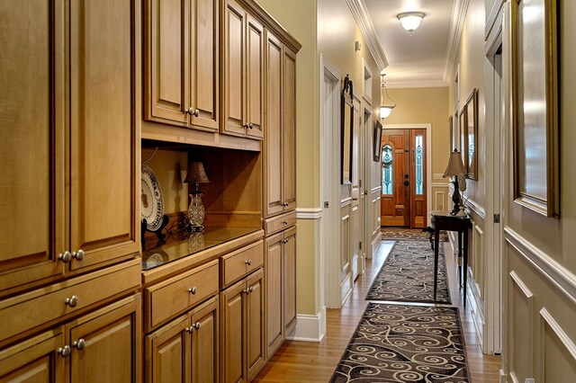 hall featuring ornamental molding, light wood-style floors, and a decorative wall