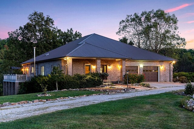 view of front of home with metal roof, an attached garage, brick siding, driveway, and a front lawn