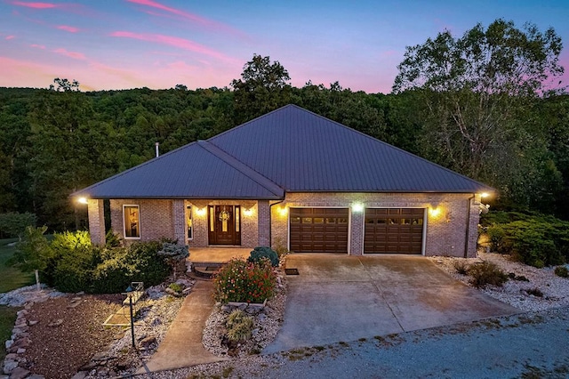 view of front of home featuring a garage, metal roof, concrete driveway, and brick siding