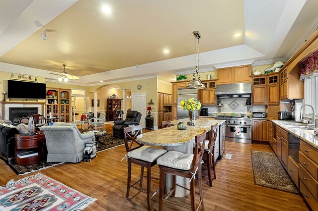 kitchen featuring wall chimney range hood, a tray ceiling, open floor plan, and premium appliances