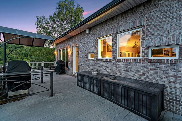 patio terrace at dusk featuring a wooden deck and a grill