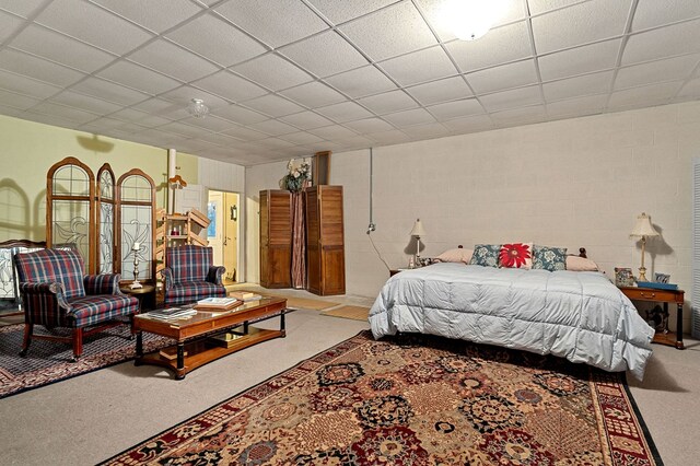 carpeted bedroom with concrete block wall and a drop ceiling