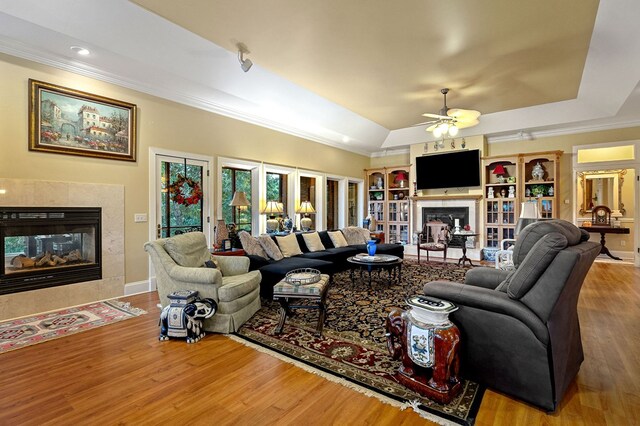 living area featuring ornamental molding, a raised ceiling, a fireplace, and wood finished floors