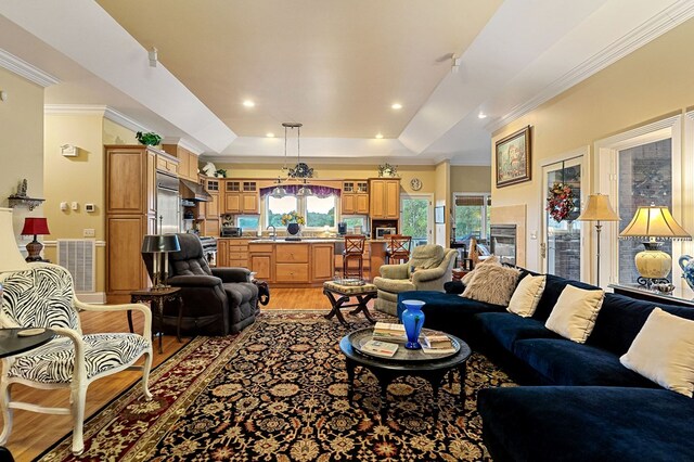 living room with recessed lighting, visible vents, light wood finished floors, ornamental molding, and a tray ceiling