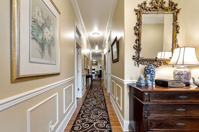 hall featuring dark wood finished floors, a decorative wall, crown molding, and wainscoting