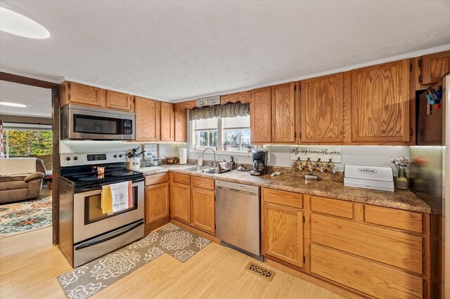 kitchen featuring visible vents, appliances with stainless steel finishes, brown cabinets, light wood-style floors, and a sink