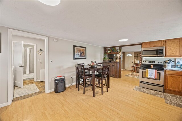 kitchen with appliances with stainless steel finishes, brown cabinetry, light wood-style floors, a textured ceiling, and baseboards