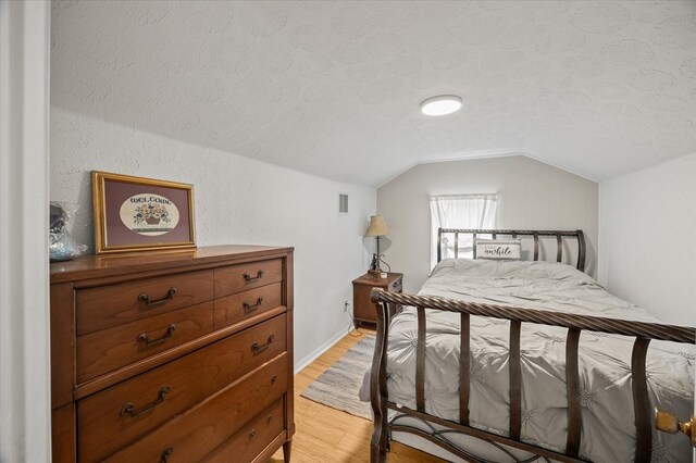 bedroom with light wood-type flooring, visible vents, vaulted ceiling, and a textured ceiling