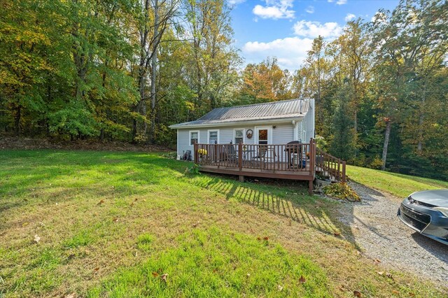 rear view of house featuring metal roof, a yard, a wooden deck, and driveway