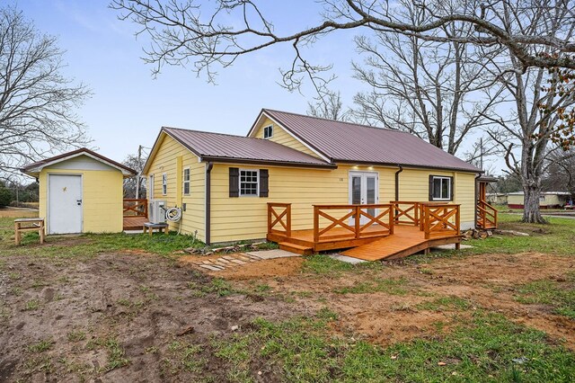 rear view of house with a deck, metal roof, an outdoor structure, french doors, and a storage unit