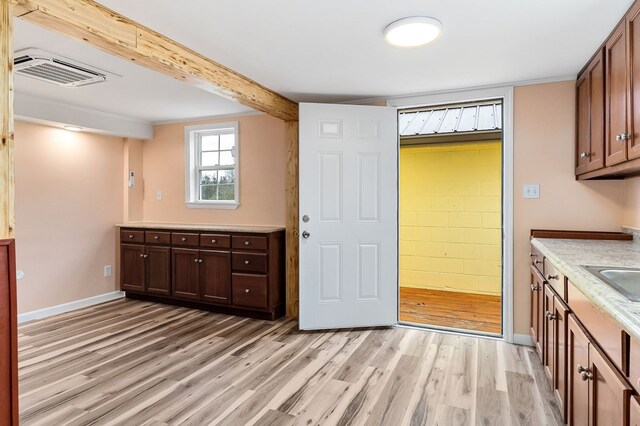 kitchen with visible vents, baseboards, light countertops, light wood finished floors, and beamed ceiling