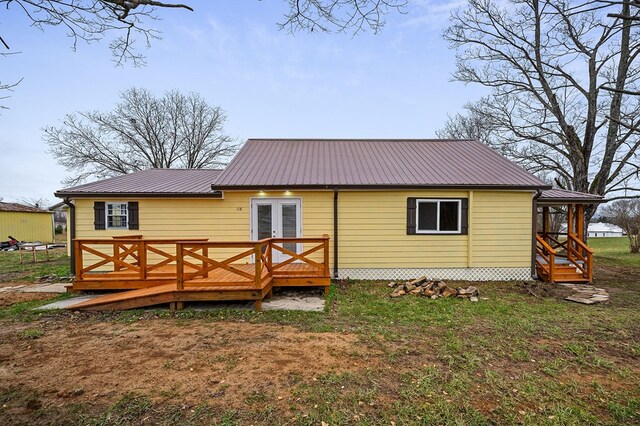 rear view of property featuring metal roof, a wooden deck, and a lawn