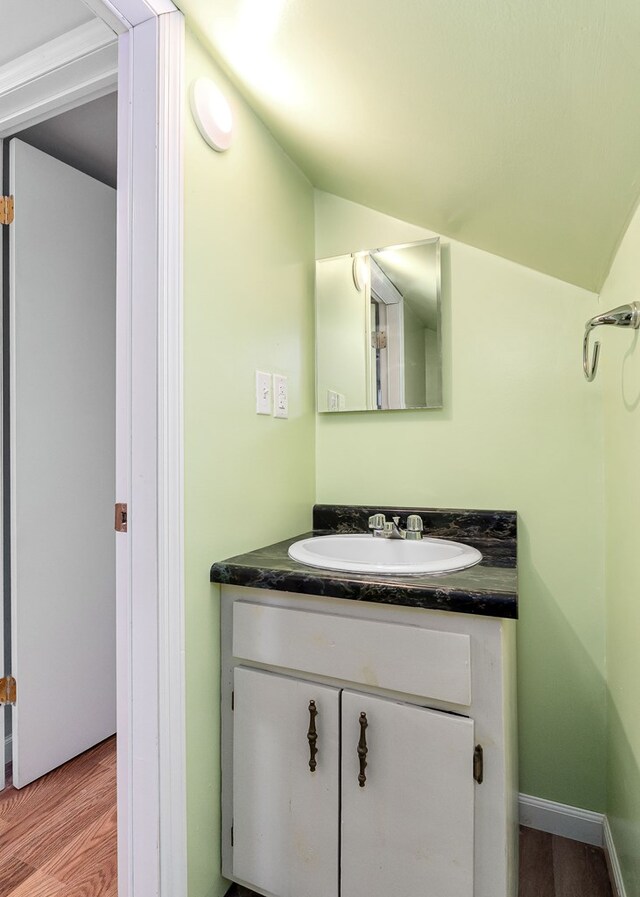 bathroom with lofted ceiling, baseboards, wood finished floors, and vanity