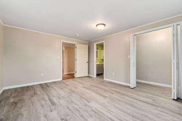 unfurnished bedroom featuring light wood finished floors, ensuite bath, baseboards, and ornamental molding