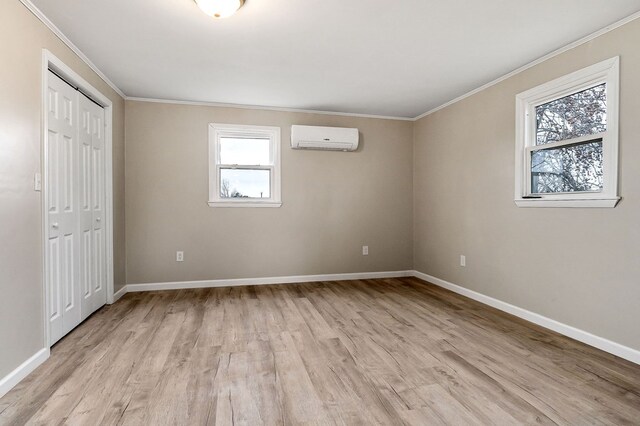 unfurnished bedroom with a wall unit AC, light wood finished floors, baseboards, and crown molding