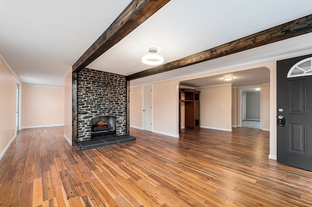 unfurnished living room with ornamental molding, a large fireplace, wood finished floors, beamed ceiling, and baseboards