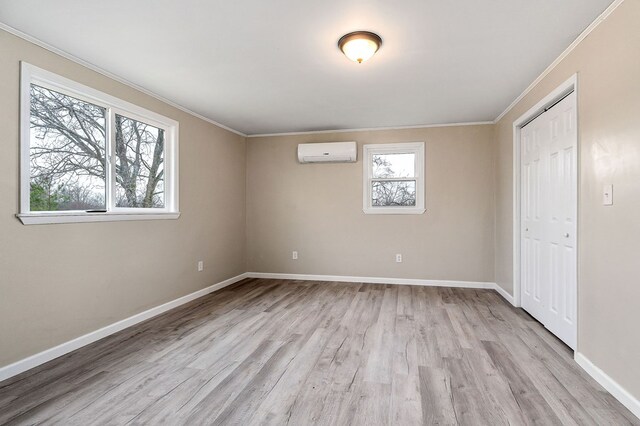 unfurnished bedroom featuring baseboards, an AC wall unit, a closet, light wood-type flooring, and crown molding