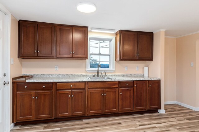 kitchen with baseboards, light stone counters, ornamental molding, light wood-style floors, and a sink