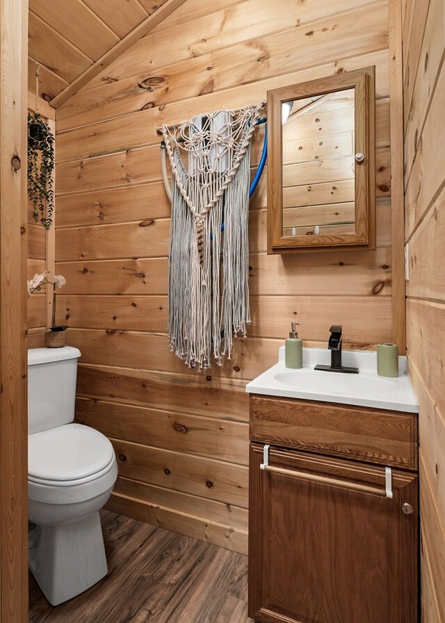 bathroom with wood walls, toilet, lofted ceiling, wood finished floors, and vanity