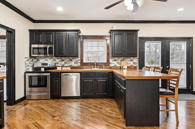 kitchen featuring a breakfast bar area, a sink, appliances with stainless steel finishes, light wood-type flooring, and tasteful backsplash