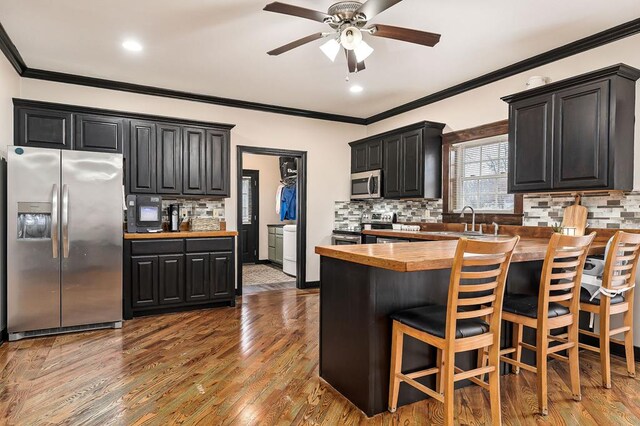 kitchen with stainless steel appliances, butcher block countertops, a sink, wood finished floors, and dark cabinetry