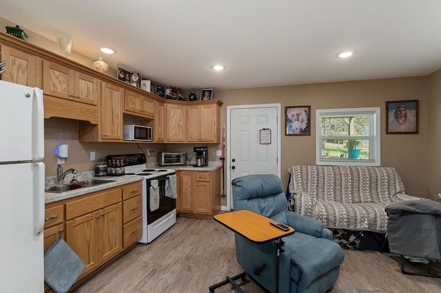 kitchen with light wood finished floors, light countertops, open floor plan, a sink, and white appliances