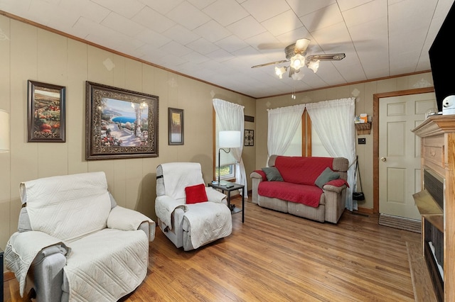 living area featuring ceiling fan, a fireplace, wood finished floors, and crown molding