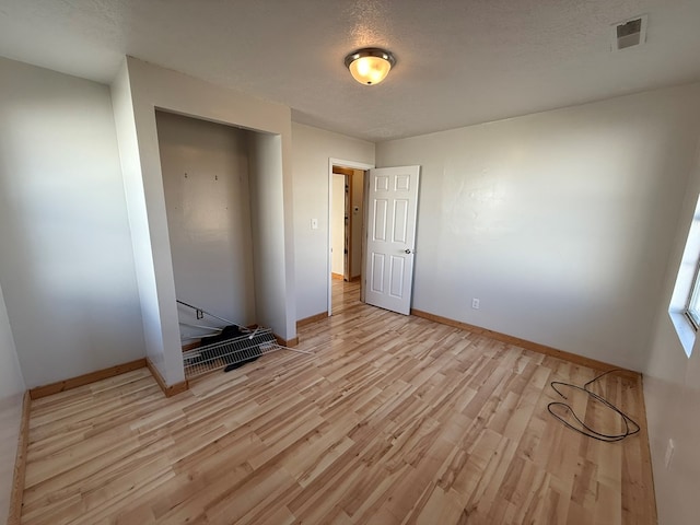 unfurnished bedroom with baseboards, visible vents, a textured ceiling, and light wood finished floors