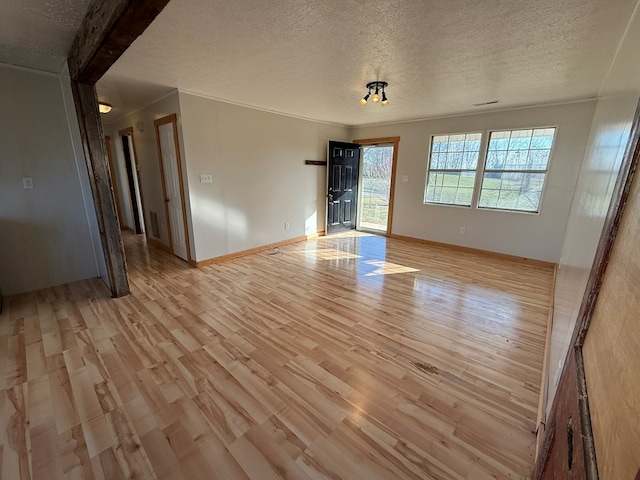 unfurnished room featuring light wood-type flooring, baseboards, visible vents, and a textured ceiling