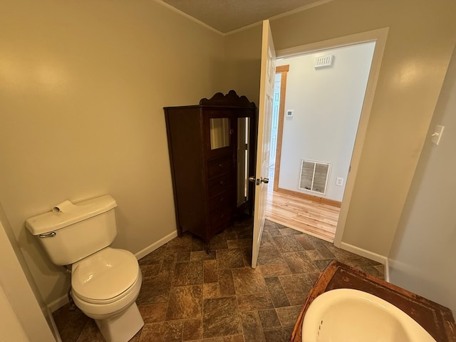 bathroom featuring toilet, stone finish flooring, visible vents, and baseboards