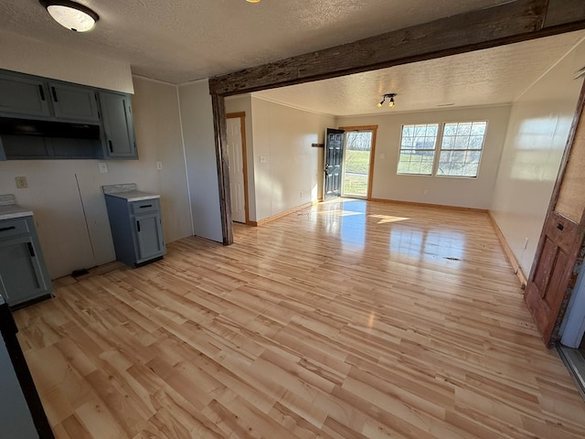 kitchen with light wood finished floors, baseboards, beamed ceiling, light countertops, and a textured ceiling