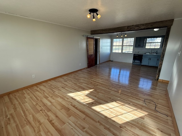 unfurnished living room featuring a textured ceiling, light wood finished floors, a sink, and baseboards