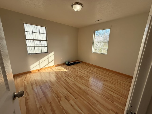 empty room with light wood-style floors, visible vents, and baseboards