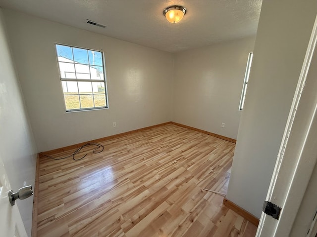 spare room with a textured ceiling, light wood finished floors, visible vents, and baseboards