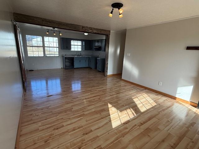 unfurnished living room featuring light wood finished floors, track lighting, baseboards, a textured ceiling, and a sink