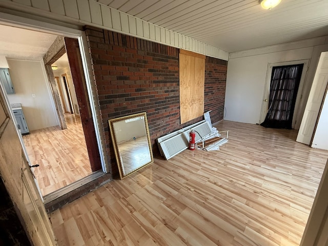 empty room featuring light wood-style floors, wooden ceiling, and brick wall