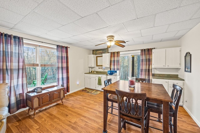 dining room featuring a drop ceiling, ceiling fan, light wood-style flooring, and baseboards