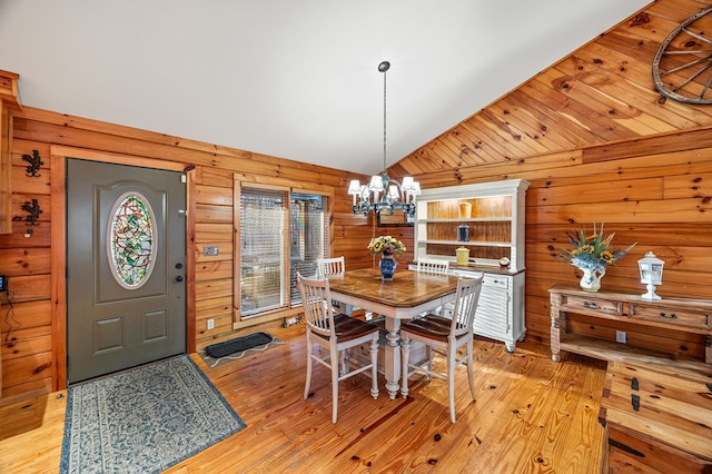 dining room with lofted ceiling, light wood-type flooring, a chandelier, and wooden walls