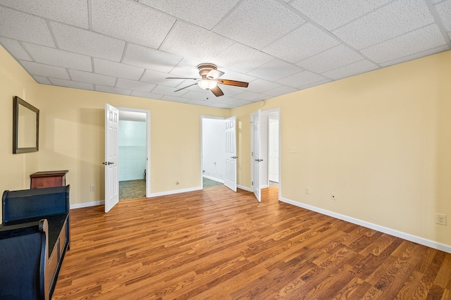 unfurnished bedroom featuring a ceiling fan, wood finished floors, a paneled ceiling, and baseboards